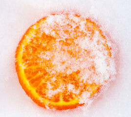 A slice of fresh frozen orange tangerine mandarin fruit cowered with white cold winter snow