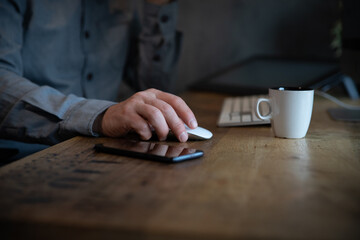 Gros plan sur la main d'un employé de bureau qui travaille sur un ordinateur. Vue sur la main qui tient la souris. On aperçoit une tasse de café, un téléphone et le clavier de l'ordinateur