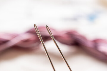 detalle de dos ojales de agujas para bordar con fondo desenfocado de hilos de algodón para bordado color guinda, mermellón