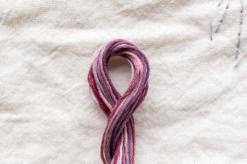 detalle de madeja de hilo de algodón para bordar trenzado colores guinda monocromático con fondo de tela de manta cruda