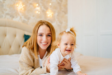Cute mom and baby daughter lie down, play and hug in bed. games with children. 