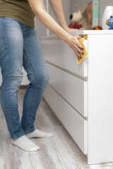 woman wipes the dust on the chest of drawers with a rag