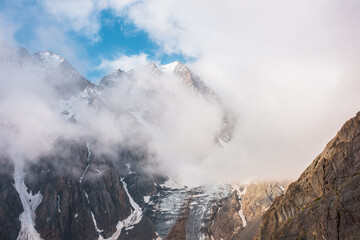 Scenic mountain landscape with snowy mountain top and glacier in dense low clouds in sunrise...