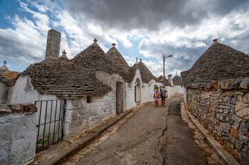 Fototapeta na wymiar Alberobello, Puglia, Italy. August 2021. Amazing view of the charming historic village. A couple of tourists walk down the alley. Beautiful summer day.