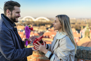 Happy couple with a gift, flowers and a balloon. The woman is surprised and overjoyed because of the beautiful gift she received from her man.