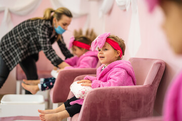 A little girl in a children's spa. She is sitting in a pink bathrobe with a big bow on her head and waiting her turn for treatment.