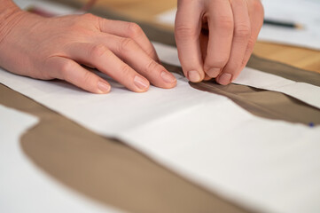 Hands of tailor with needle touching pattern on fabric