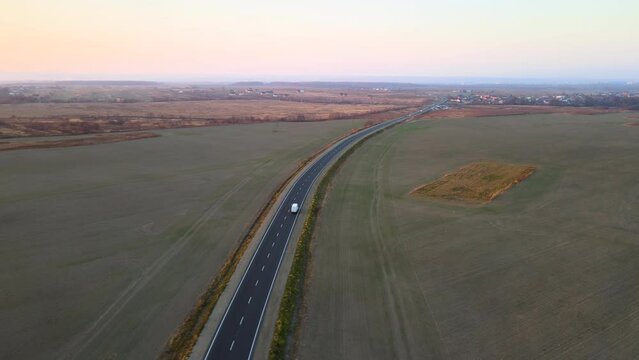 Aerial view of small cargo van driving on highway hauling goods at sunset. Delivery transportation and logistics concept
