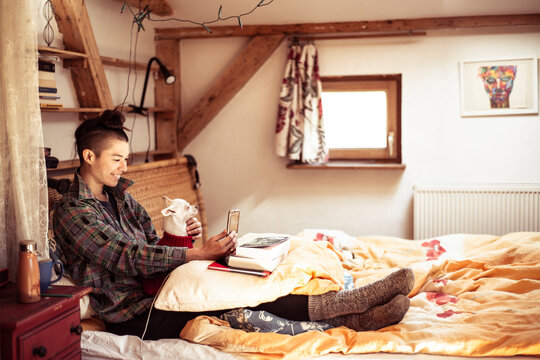 Mixed race woman sits on bed with dog and video chat's on phone