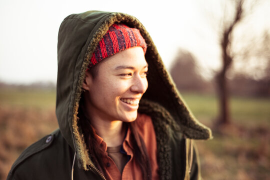 non-binary person in warm jacket hood smiles in afternoon sun outdoors