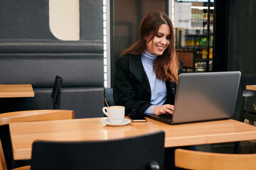 Woman working remotely with her laptop in a coffee shop
