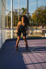 Chica morena con pelo rizado en ropa deportiva patinando en pista azul de patinaje