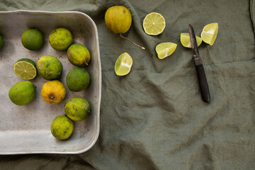 Creative still life of garden picked sliced limes in a rustic tray on a green linen towel 