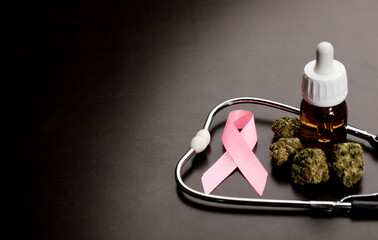 cancer pink ribbon, medical marijuana buds with stethoscope, oil bottle, brown background.