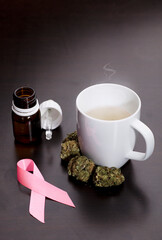 Obraz na płótnie Canvas cancer pink ribbon with marijuana buds, white cup with infusion steam, oil drops dispenser bottle, on brown table, wooden background