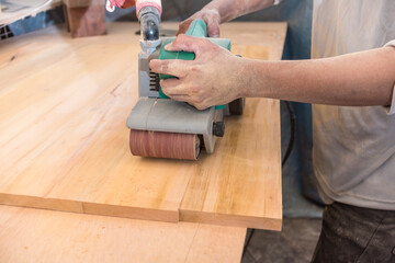 Using a hand-held sanding machine or belt sander to level the surface of a sheet of plywood for a...
