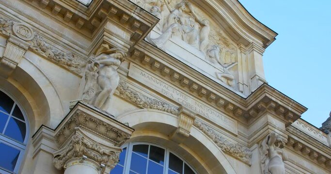 French Inscription And Sculptures On Facade Of Gobelins Manufactory, Historic Tapestry Factory In Paris, France. close up, low angle
