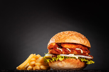 Double fried chicken burger with french fries onions cucumber and lettuce. On dark background..