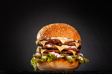 Quadruple burger with cheese cucumber and lettuce. Isolated on black background..