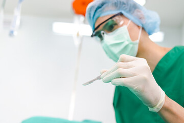 Asian professional surgeon holding a scalpel with glasses and wear gloves and a mask In the operating room in the hospital. Concept of medical services. cosmetic surgery. Copy space