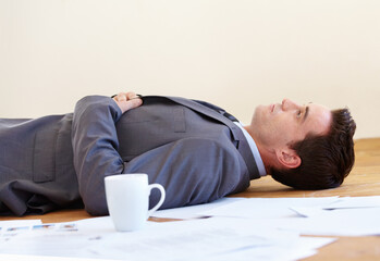 Work really takes its toll. A handsome young businessman lying on the floor of his office.