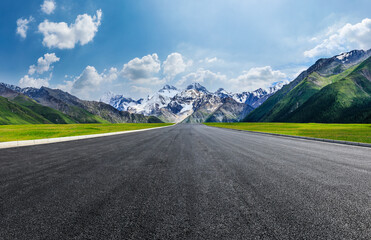 Straight asphalt road and green grass with snow mountain nature scenery under blue sky. Road and mountains background.