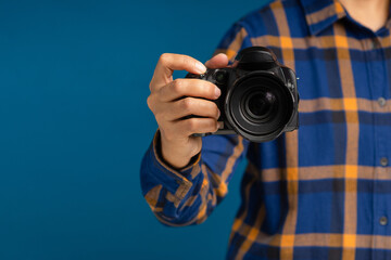 Close-up of hand holding the digital camera while standing on a blue background