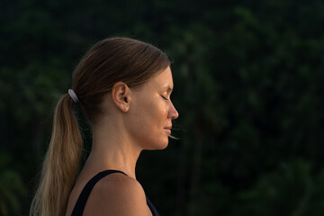 Portrait of a young woman meditating at sunrise with her eyes closed. Forest in the background .