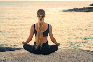 Fototapeta na wymiar Young caucasian woman with long hair meditating in a black clothes for yoga on a rocks on the top by the sea.