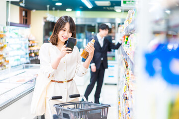 スーパーの商品をスマホで調べる若い女性