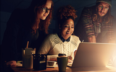 Well succeed together. Shot of a business team using a laptop together on a night shift at work.