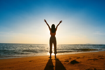 silhouette happy young woman enjoying freedom with open hands on sea at sunset