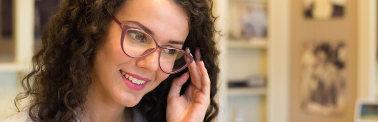 Young beautiful woman choosing eyeglasses in optical shop.