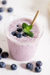 Glass of blueberry milkshake with fresh blueberries on white wooden background.