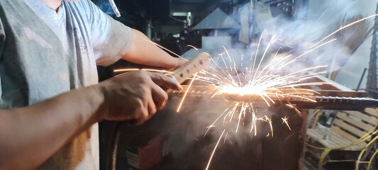 A man is welding steel in a factory. At night there was fire and smoke everywhere.