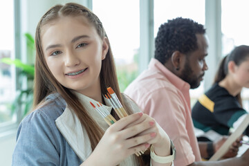 Close-up student caucasoid girl smile and holding paint brush learning in art classroom. education art concept.