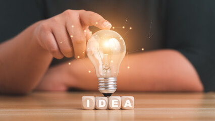 idea concept with innovation and inspiration.Female hand holding a lightbulb light bulb on wood block with Word Ideas.