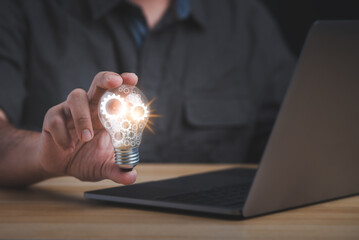 The hand of a man with a light bulb and he is using a laptop. The idea of ​​inspiration from online technology.innovation idea concept.
