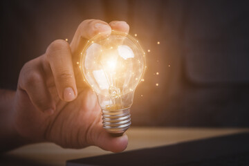 Businessman hand holding light bulb and using laptop on wooden table. new idea creativity concept with innovation and inspiration.