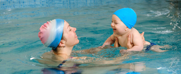 Early age swimming in pool. Baby boy trained to swim in water. Happy child with trainer woman in...