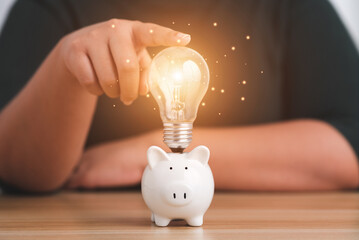 Save money and inspiration. Female hand holding a light bulb and a white piggy bank.