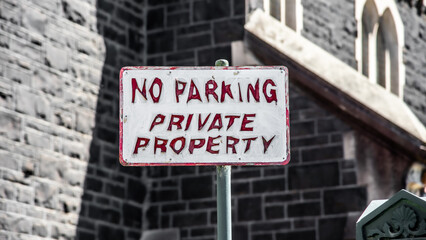 A red and white No Parking sign with letters that have faded and peeled to give an unintentional evil looking font