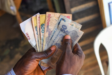 Hands holding spread of multiple Nigerian naira notes, cash, currency or money in an outdoor...