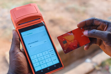 Hand of an african individual holding a point of sales terminal or POS machine with an ATM card in a market place