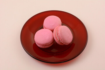 Pink raspberry French macaron cookies on red glass plate on pink background