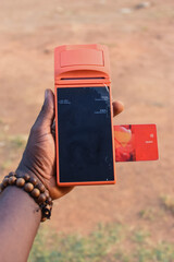 Hand of an african individual holding a point of sales terminal or POS machine with an inserted ATM...