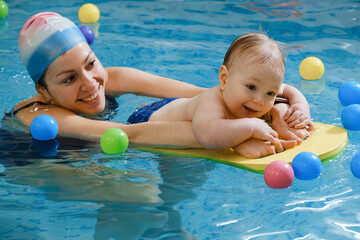 Early age swimming in pool. Baby boy trained to swim in water. Happy child with trainer woman in indoor swimming pool playing and having fun. Healthy and sport family with infant, active parent