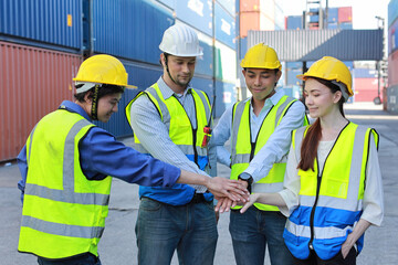 Group of multiethnic technician engineer and businessman in protective uniform with hardhat stand and stacking hands celebrate successful together or completed deal commitment at container cargo site