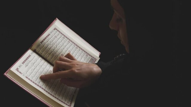 A Muslim woman reading the noble Quran and tracing the Quranic verses with her finger