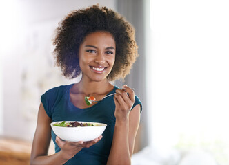 Getting her greens. Portrait of an attractive young woman eating a bowl of salad. - Powered by Adobe